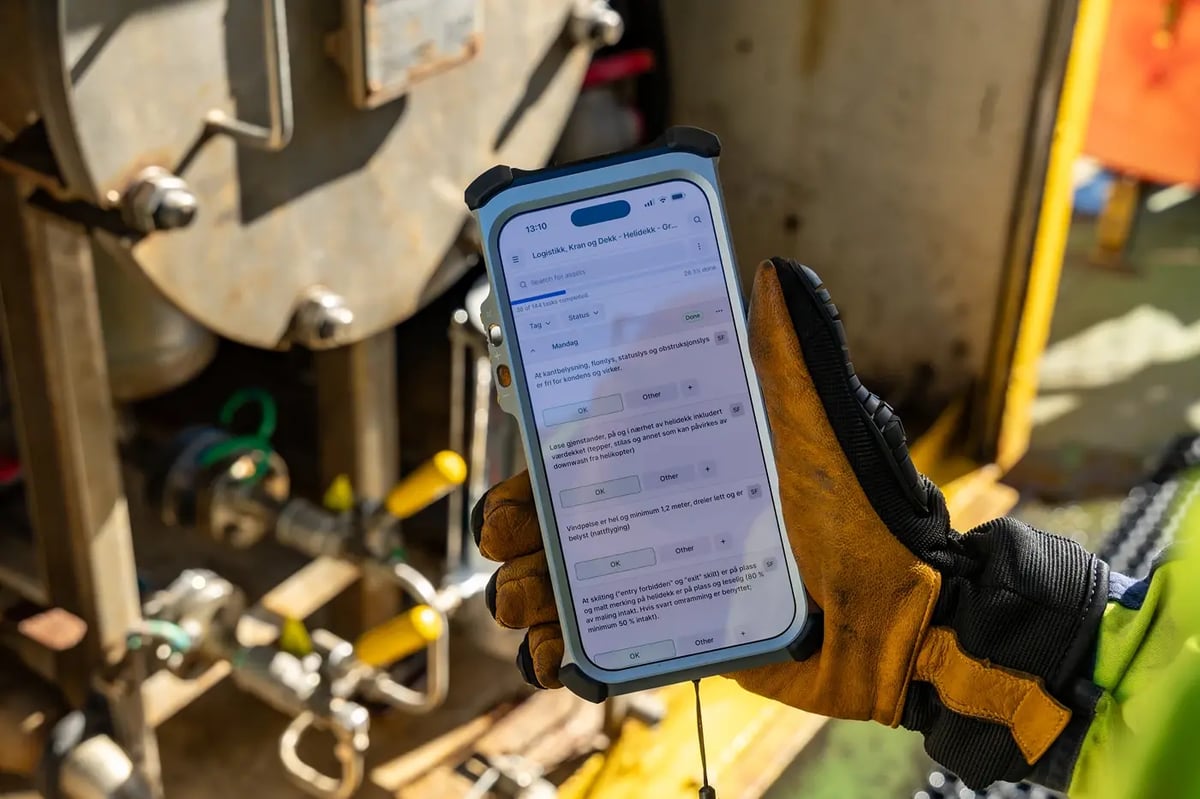 Gloved operator holding an explosion-proof iPhone with a digital checklist on screen