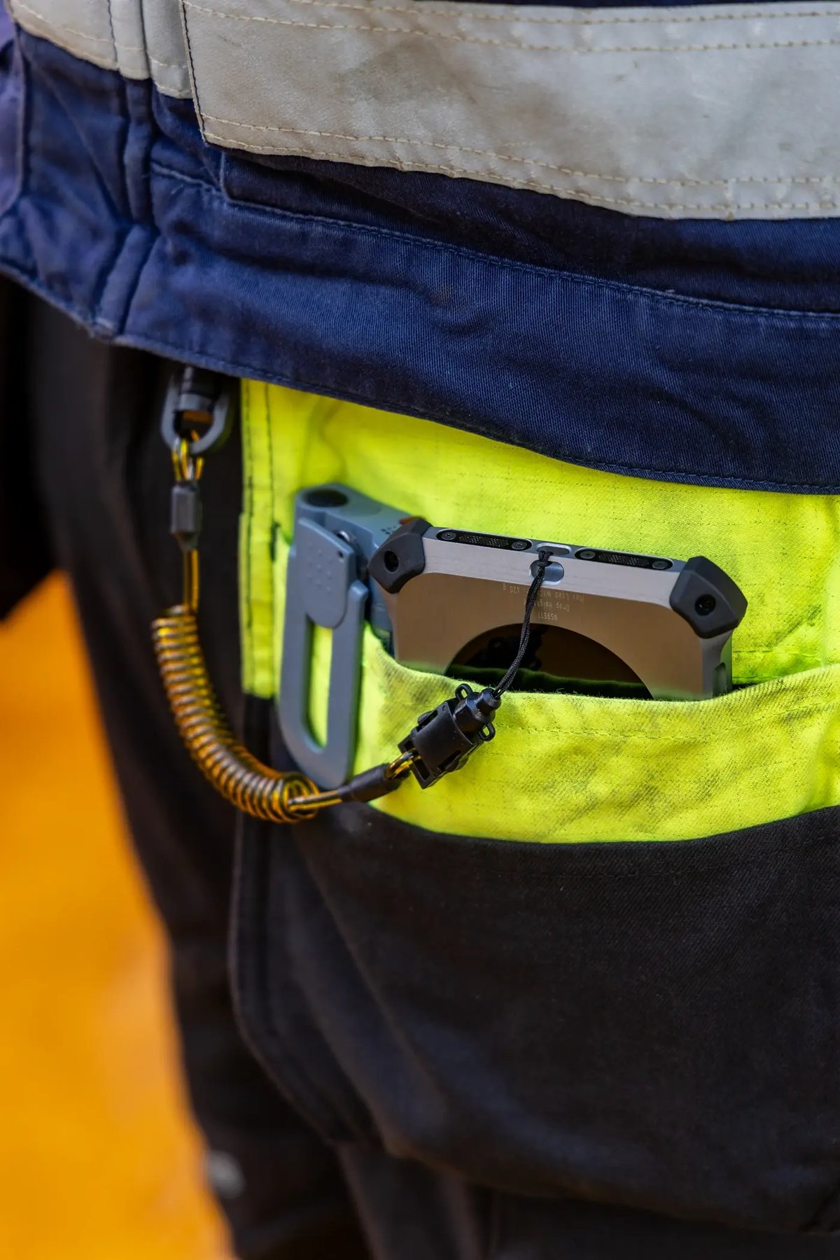 Explosion-proof iPhone clipped into a technician's coverall pocket on a lanyard